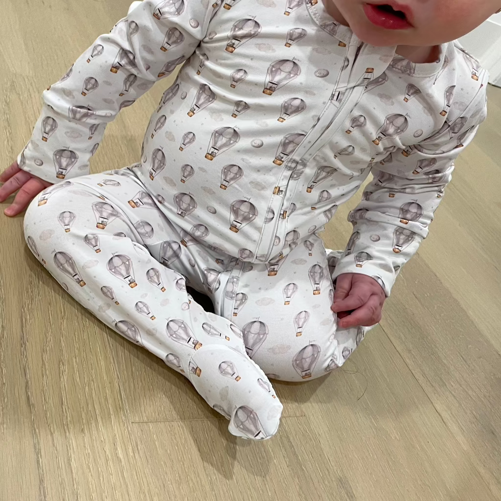 Cozy bamboo footed sleeper keeping baby snug, featuring adorable hot air balloon print.